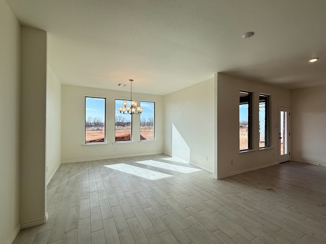 empty room with an inviting chandelier, baseboards, visible vents, and light wood finished floors