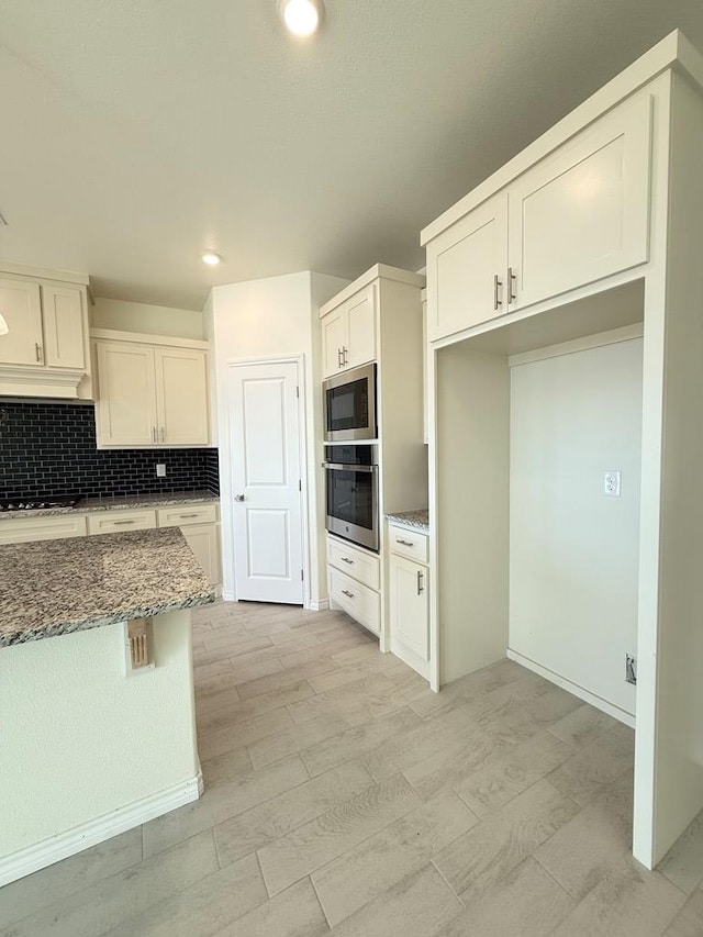 kitchen with stone counters, stainless steel appliances, recessed lighting, backsplash, and white cabinetry