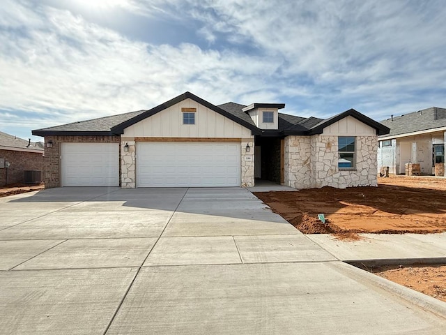 view of front of property with an attached garage, central AC, stone siding, concrete driveway, and board and batten siding