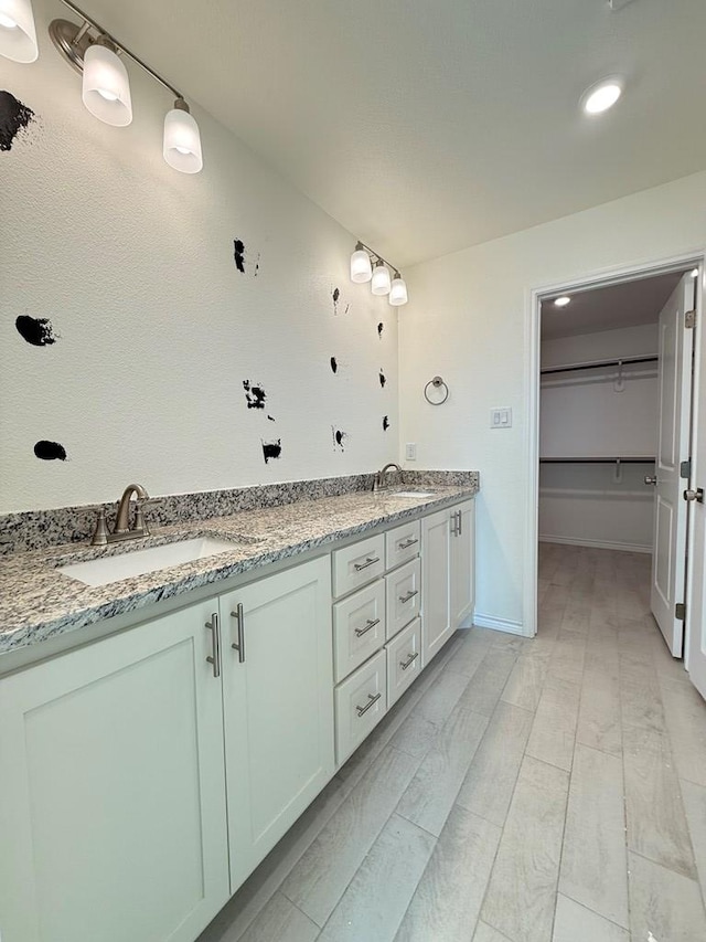 full bathroom with double vanity, a spacious closet, baseboards, and a sink