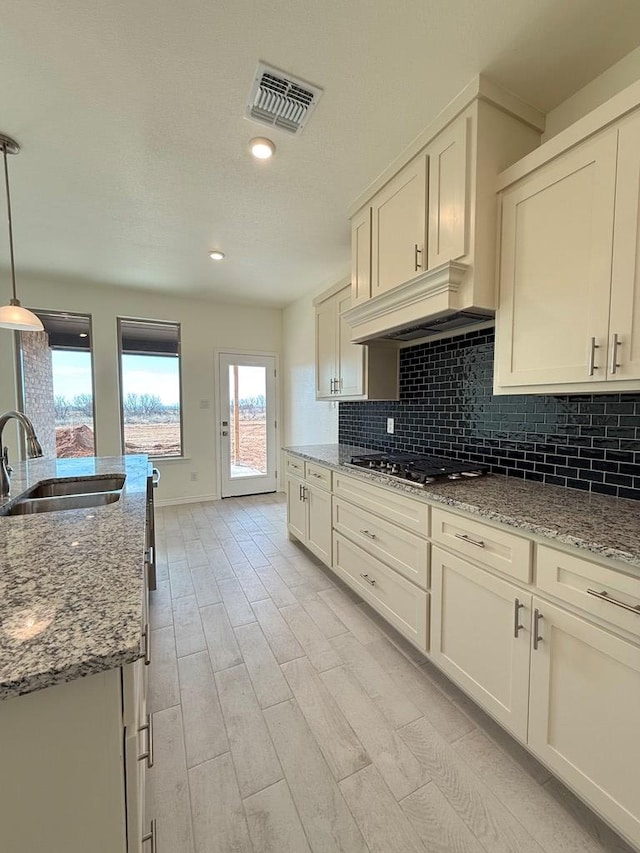 kitchen featuring stainless steel gas cooktop, a sink, visible vents, custom exhaust hood, and backsplash