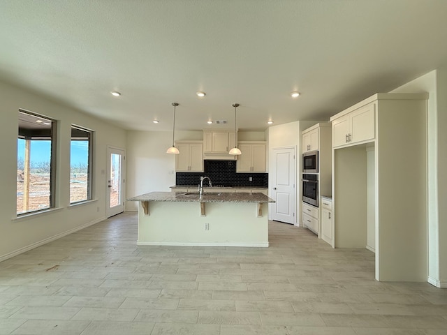 kitchen with a breakfast bar, a kitchen island with sink, stainless steel appliances, stone counters, and backsplash