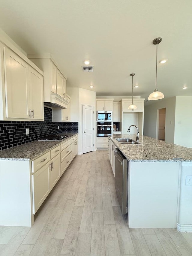 kitchen featuring light wood finished floors, visible vents, decorative backsplash, appliances with stainless steel finishes, and a sink