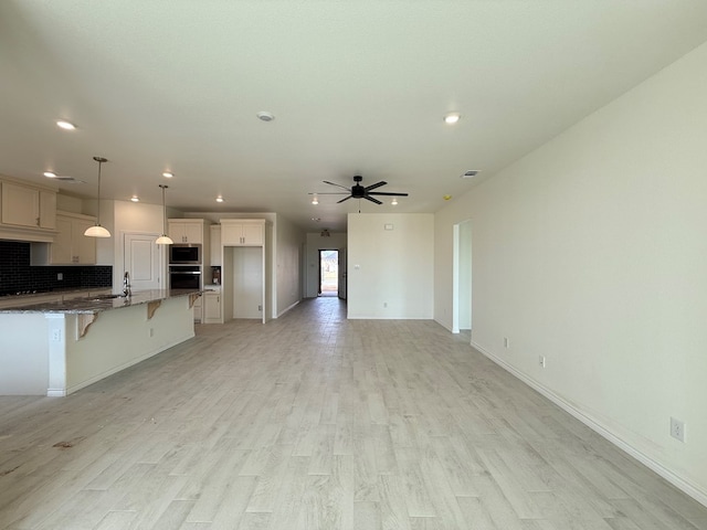 kitchen with stainless steel appliances, light wood-style flooring, a ceiling fan, a sink, and a kitchen breakfast bar