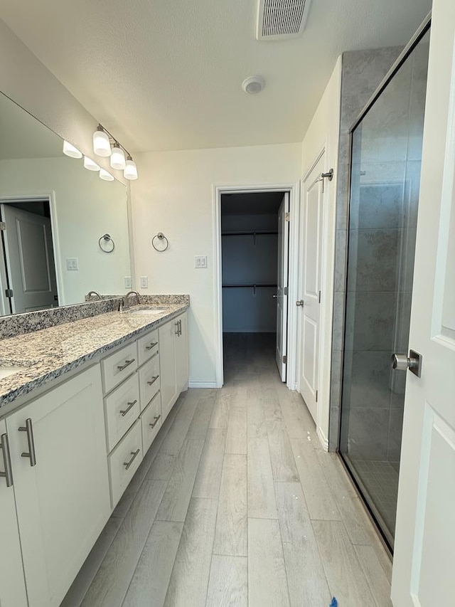 full bathroom with double vanity, visible vents, a shower stall, and wood finished floors