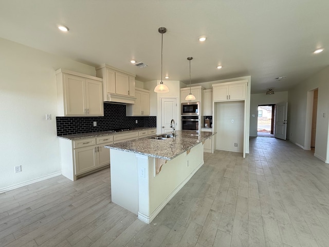 kitchen with light wood finished floors, stainless steel appliances, decorative backsplash, stone countertops, and a sink