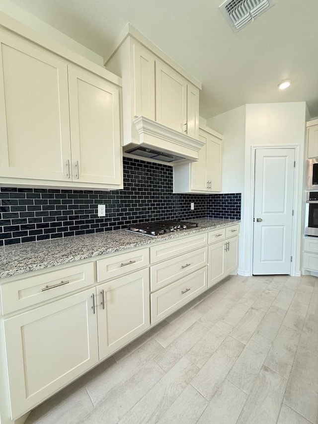 kitchen with light stone counters, stainless steel appliances, visible vents, backsplash, and premium range hood