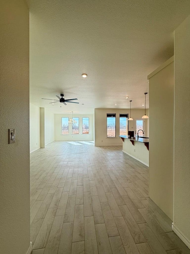 unfurnished living room featuring a ceiling fan, light wood-type flooring, a sink, and a textured wall