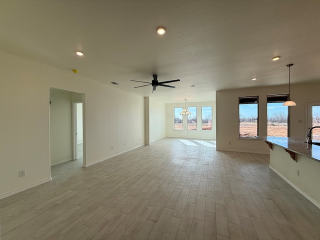 unfurnished living room with light wood-style floors, recessed lighting, baseboards, and ceiling fan with notable chandelier