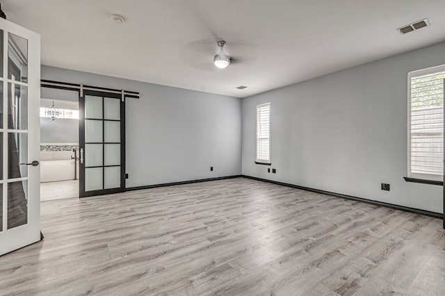 unfurnished room featuring a ceiling fan, visible vents, wood finished floors, a barn door, and baseboards