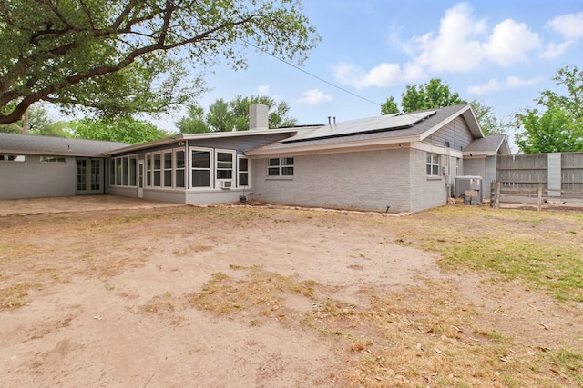 rear view of house featuring a chimney, brick siding, fence, cooling unit, and roof mounted solar panels