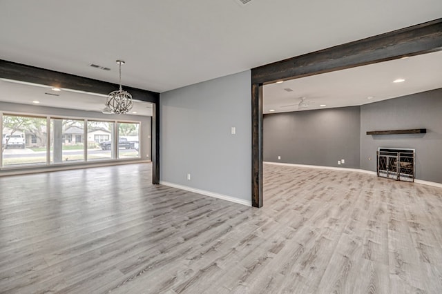 unfurnished living room featuring visible vents, a fireplace, wood finished floors, baseboards, and an inviting chandelier