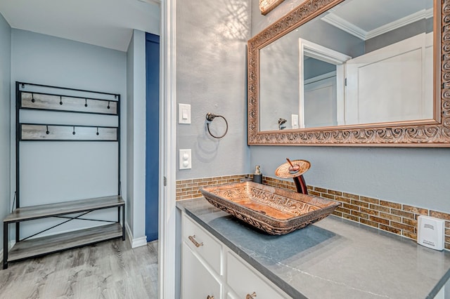 bathroom featuring backsplash, crown molding, wood finished floors, vanity, and baseboards