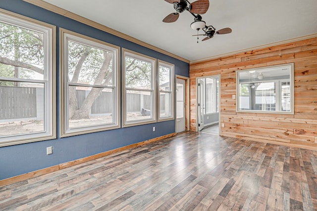 unfurnished room with a healthy amount of sunlight, a ceiling fan, and wooden walls