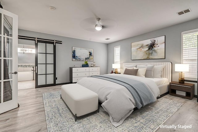 bedroom with a barn door, visible vents, multiple windows, and wood finished floors