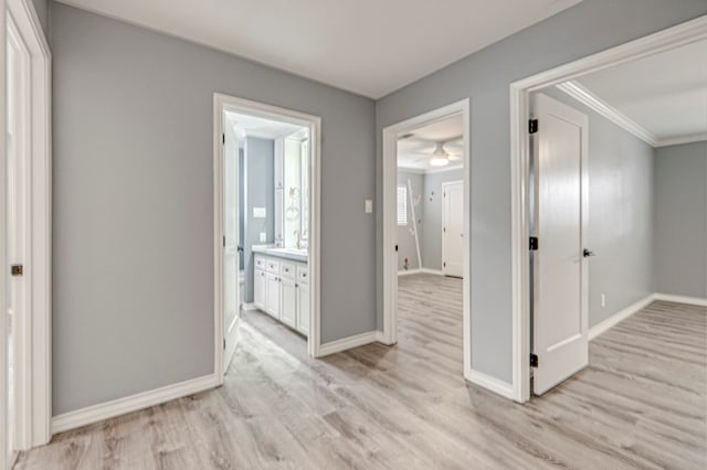 interior space with light wood-style floors, baseboards, crown molding, and connected bathroom