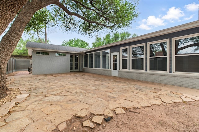 back of property with brick siding, fence, a sunroom, and a patio