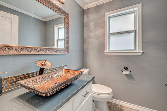 half bathroom with crown molding, a healthy amount of sunlight, toilet, and vanity