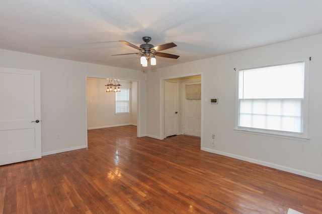 empty room with ceiling fan with notable chandelier, a wealth of natural light, and dark hardwood / wood-style floors