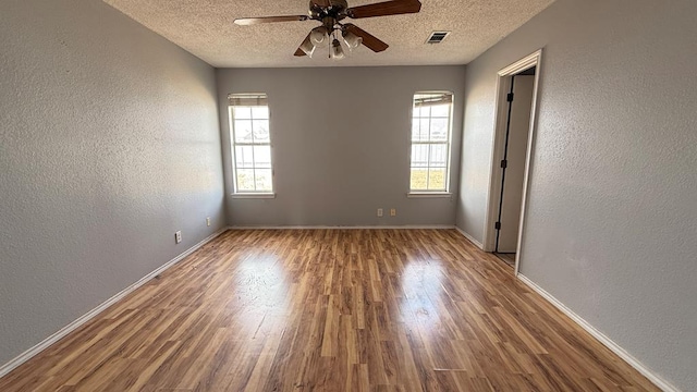 empty room with visible vents, wood finished floors, and a textured wall