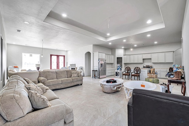 living area with recessed lighting, a tray ceiling, arched walkways, and visible vents