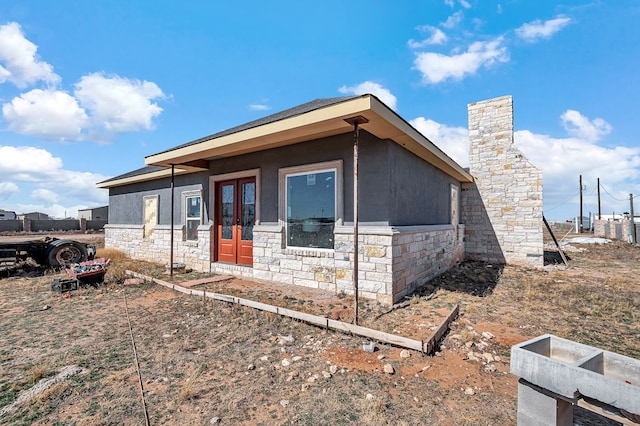 view of front of property featuring stucco siding, stone siding, a chimney, and french doors