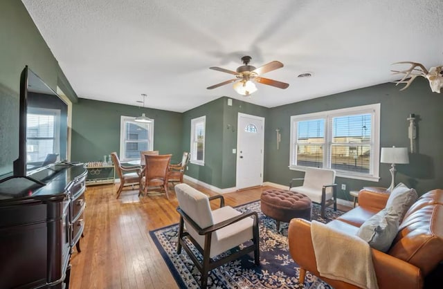 living area with a textured ceiling, a ceiling fan, visible vents, baseboards, and light wood-type flooring