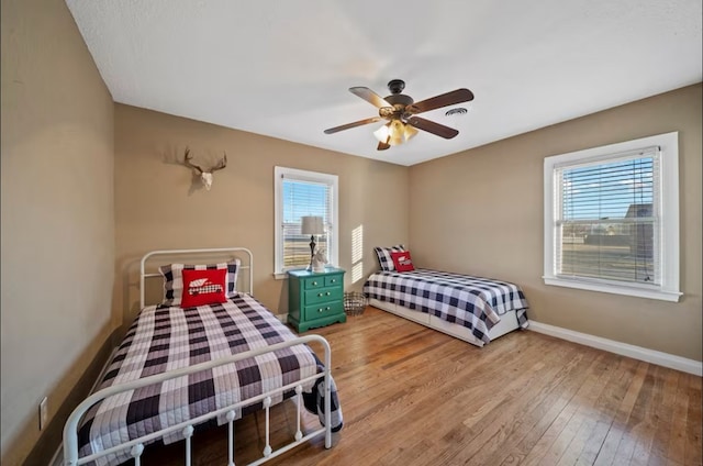 bedroom with light wood finished floors, a ceiling fan, visible vents, and baseboards