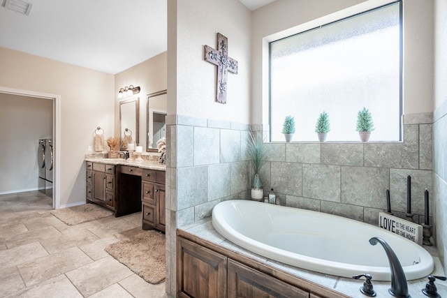 bathroom with vanity, tiled bath, and washing machine and clothes dryer