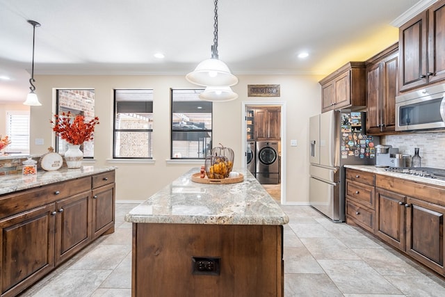 kitchen featuring decorative light fixtures, a center island, light stone counters, stainless steel appliances, and washer and clothes dryer