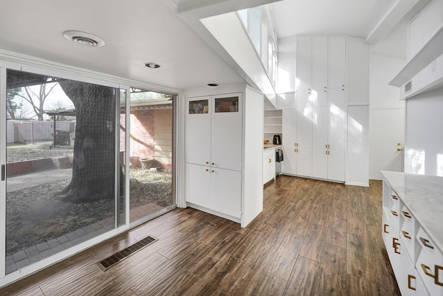 interior space with dark wood-style flooring, light stone countertops, visible vents, and white cabinetry