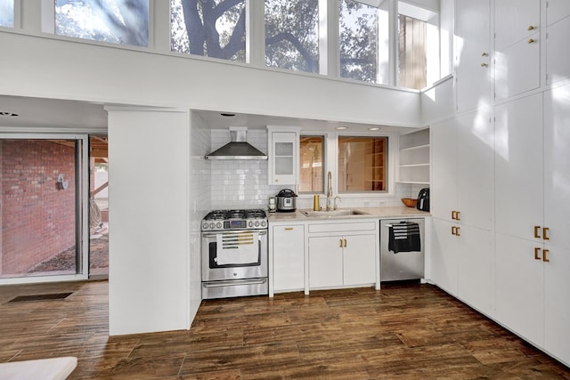 kitchen featuring dark wood-style flooring, stainless steel appliances, white cabinets, a sink, and wall chimney range hood