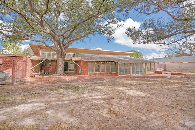 back of house with brick siding, fence, and a sunroom