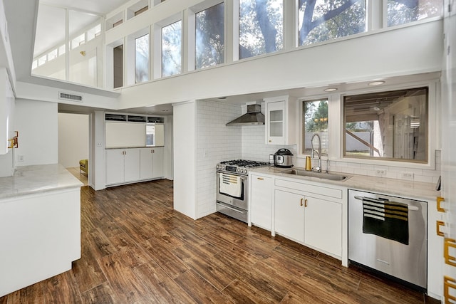 kitchen featuring white cabinets, wall chimney exhaust hood, appliances with stainless steel finishes, dark wood-style flooring, and a sink