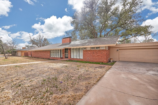 ranch-style home featuring brick siding, driveway, a chimney, and an attached garage