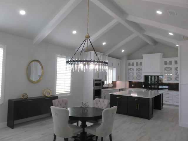 dining room featuring vaulted ceiling with beams, light wood-type flooring, and sink