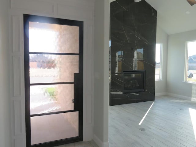 doorway with a fireplace, light hardwood / wood-style flooring, and lofted ceiling