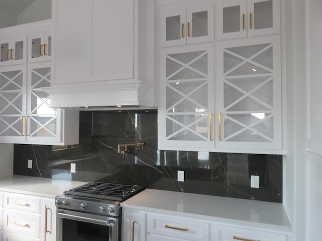 kitchen with stainless steel range, backsplash, ventilation hood, and white cabinetry