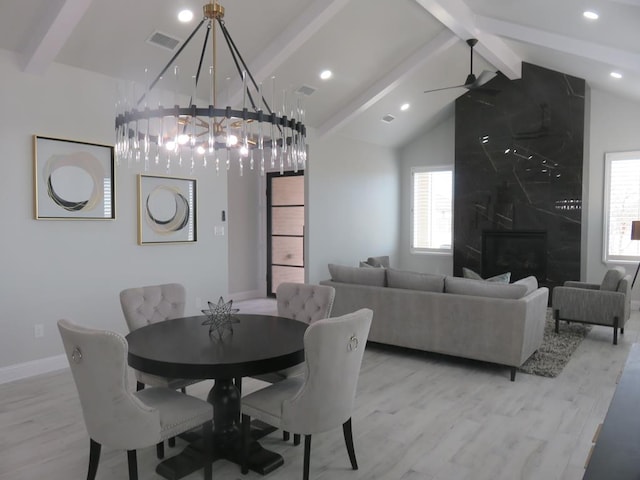 dining space featuring lofted ceiling with beams, a fireplace, light hardwood / wood-style floors, and ceiling fan with notable chandelier