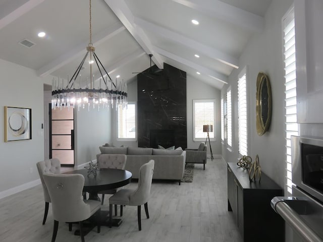 dining space featuring a chandelier, lofted ceiling with beams, light hardwood / wood-style flooring, and a premium fireplace