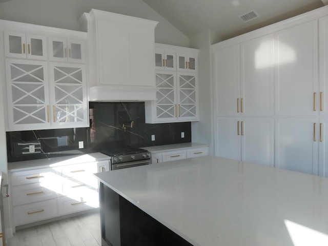 kitchen with white cabinets, backsplash, high end range, and lofted ceiling