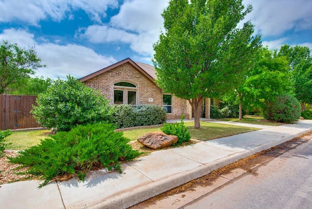 view of front facade featuring fence, a front lawn, driveway, and brick siding