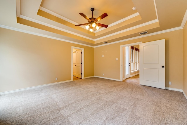 empty room featuring light colored carpet, a raised ceiling, and crown molding