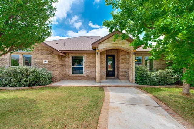 single story home featuring a front yard, roof with shingles, and brick siding
