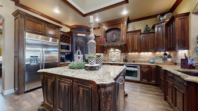 kitchen featuring built in appliances, ornamental molding, a sink, a center island with sink, and tasteful backsplash