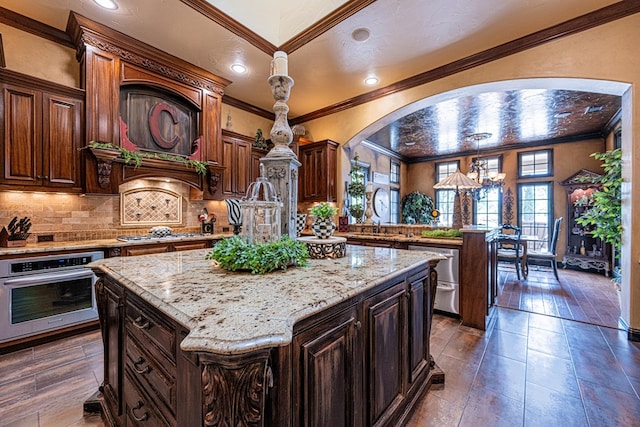 kitchen with stainless steel appliances, crown molding, a center island, backsplash, and decorative light fixtures