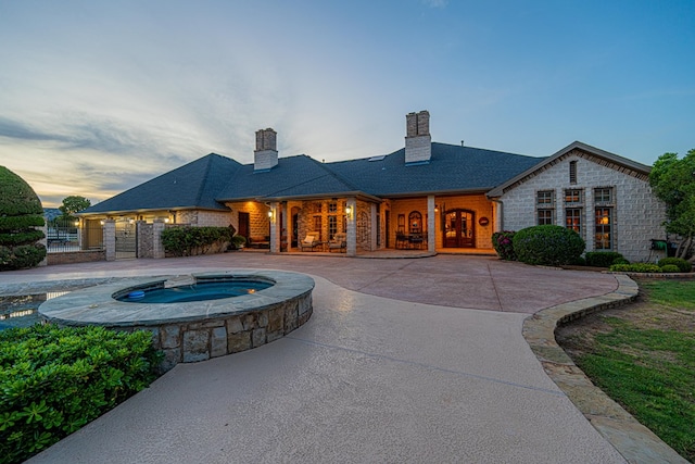 rear view of property featuring a chimney, stone siding, fence, and a pool with connected hot tub