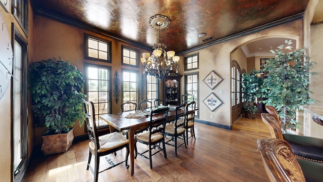 dining room featuring arched walkways, a chandelier, ornamental molding, baseboards, and hardwood / wood-style flooring
