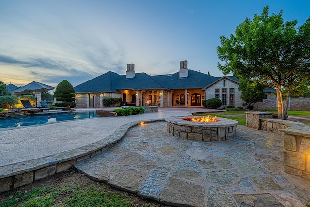 pool at dusk featuring a patio area, a fire pit, and an outdoor pool