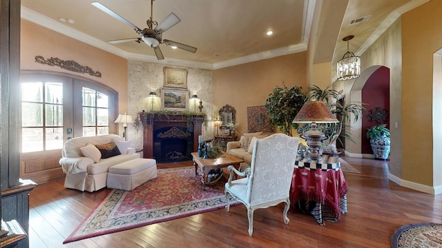 living room with arched walkways, hardwood / wood-style floors, a ceiling fan, a fireplace, and crown molding